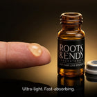 Light water-based serum drop on a fingertip beside a Roots & Ends vial